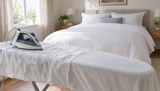 Bettwäsche bügeln: Bügelbrett mit Bügeleisen und weißem Bettbezug vor einem frisch bezogenen Bett