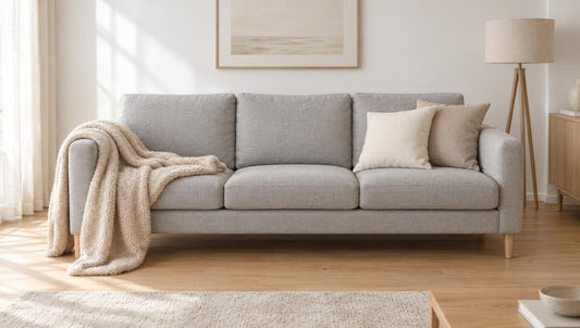 Beige Sofadecke locker über die Armlehne eines hellgrauen Sofas drapiert